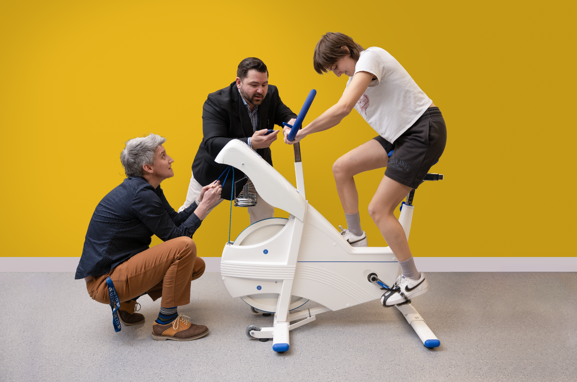 two faculty members encourage student on exercise bike